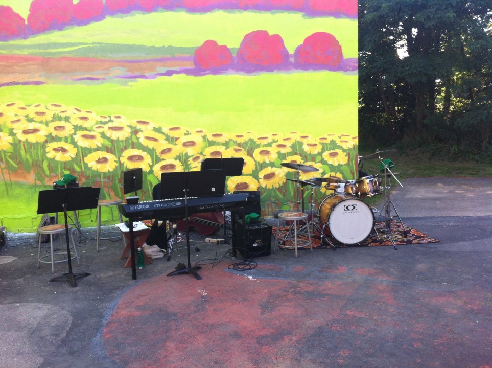 Image of a drum set against a mural of a landscape with sunflowers and corn files.